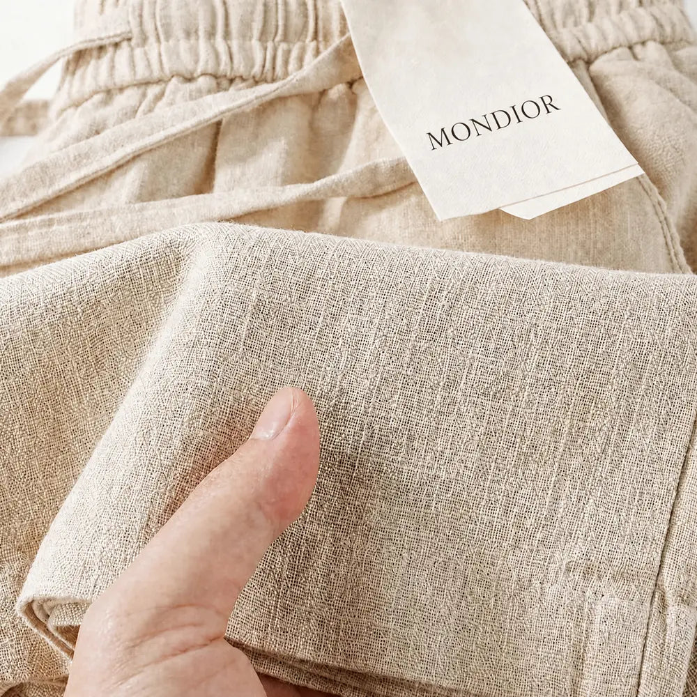 Detalhe aproximado da textura autêntica da calça feminina em linho italiano capri bege, com foco no acabamento das costuras e na trama do tecido.
